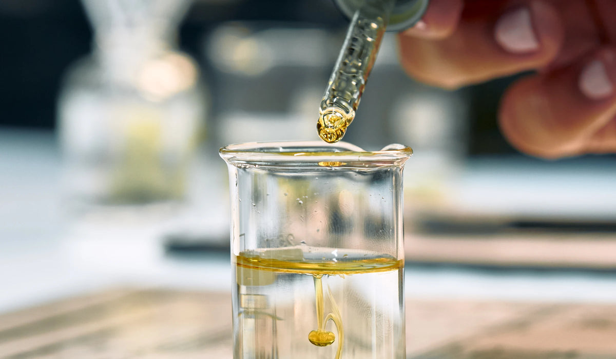 Golden fragrance dropping into a glass beaker, photographed for Oo La Lab by Trigger